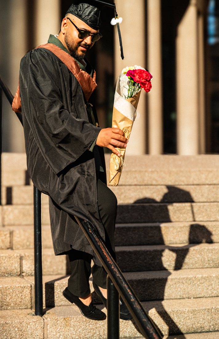 Graduate carrying carnations down stone steps, his shadow thrown on the wall