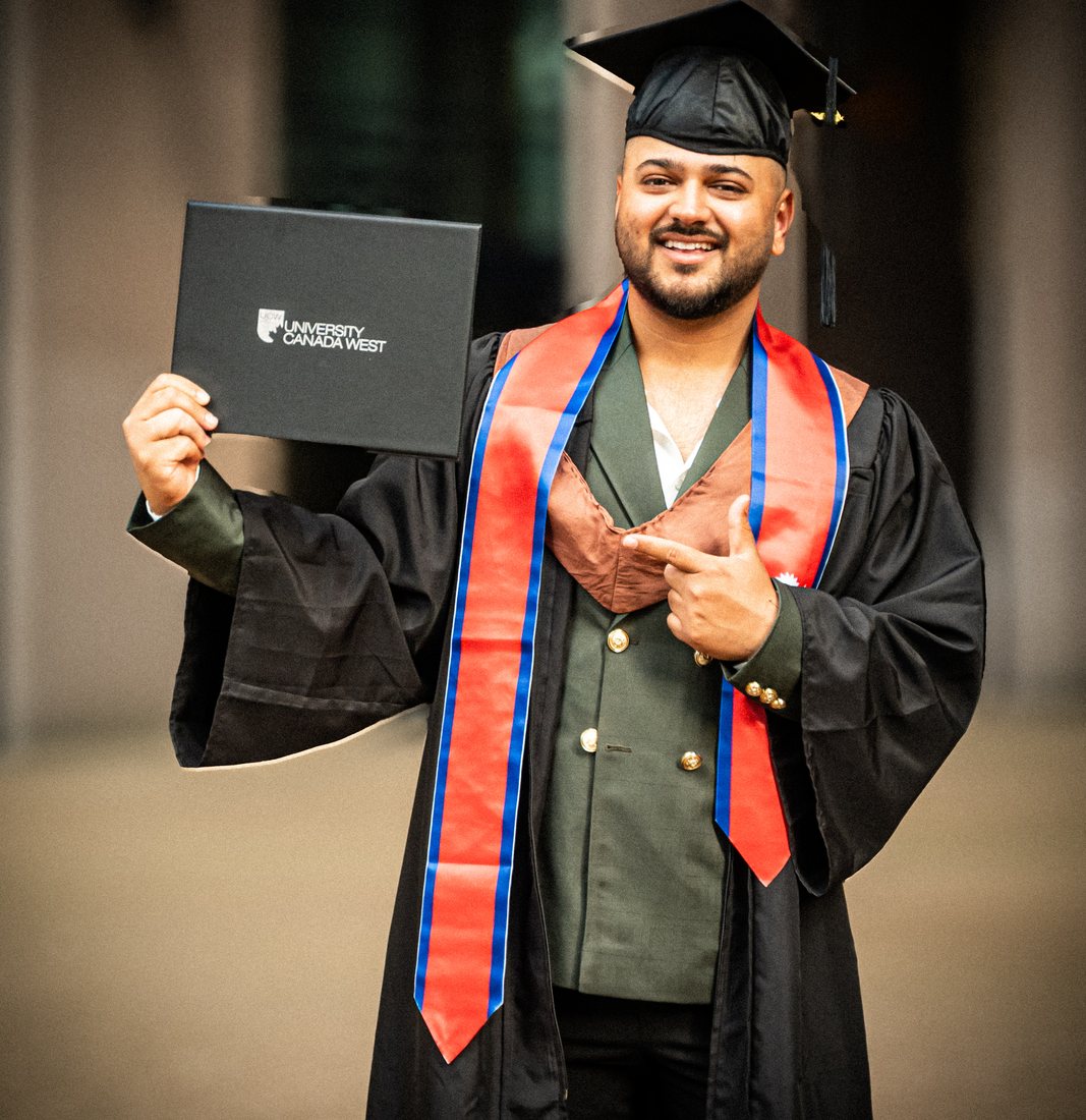Graduate holding his degree, red stole against a dark gown, library columns behind