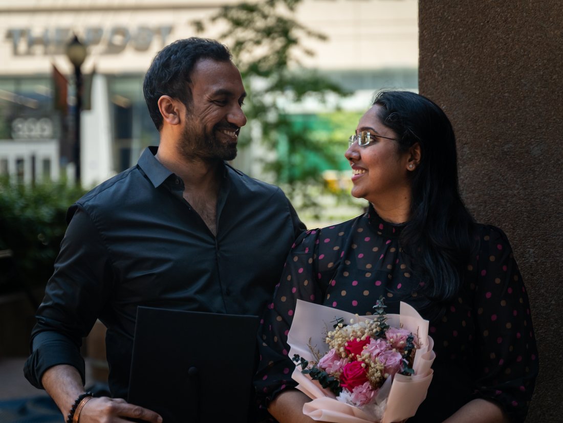 Graduate and her partner smiling at each other in open shade downtown