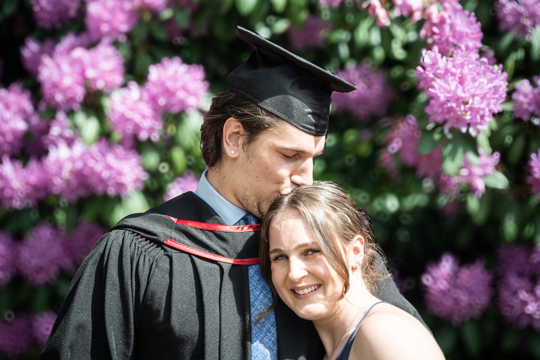 Graduate kissing his partner's hair among pink rhododendrons at UBC