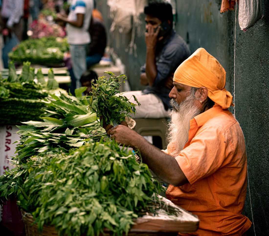 Vegetable vendor in an orange turban at his stall, surrounded by greens