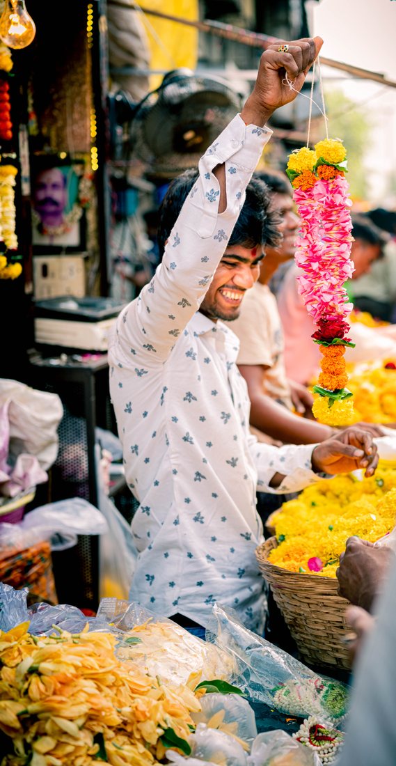 Flower seller reaching up for a garland above baskets of yellow flowers