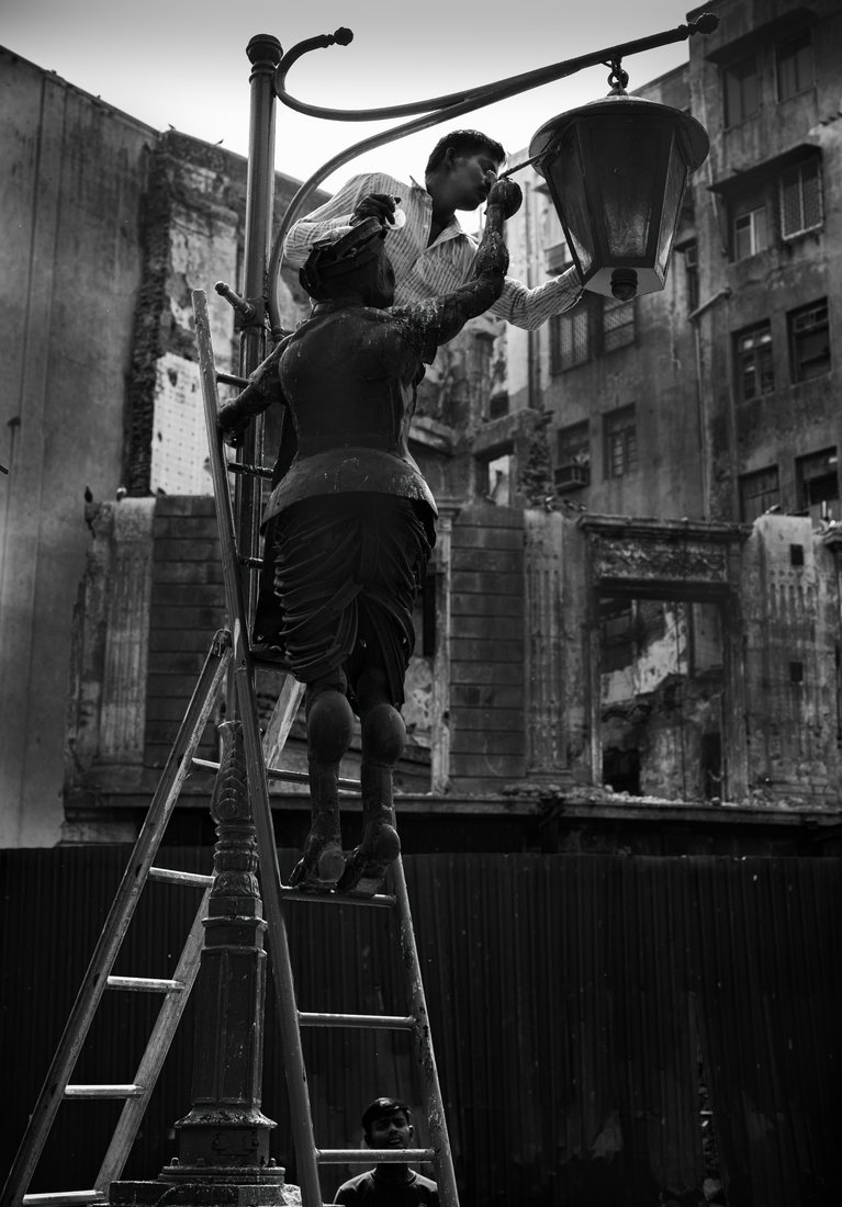 Man on a ladder working on a street lantern against a painted wall, toned monochrome