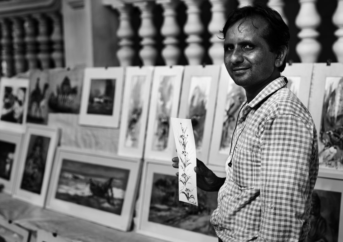 Dhammapal Kirdak smiling beside his prints at a street market, monochrome