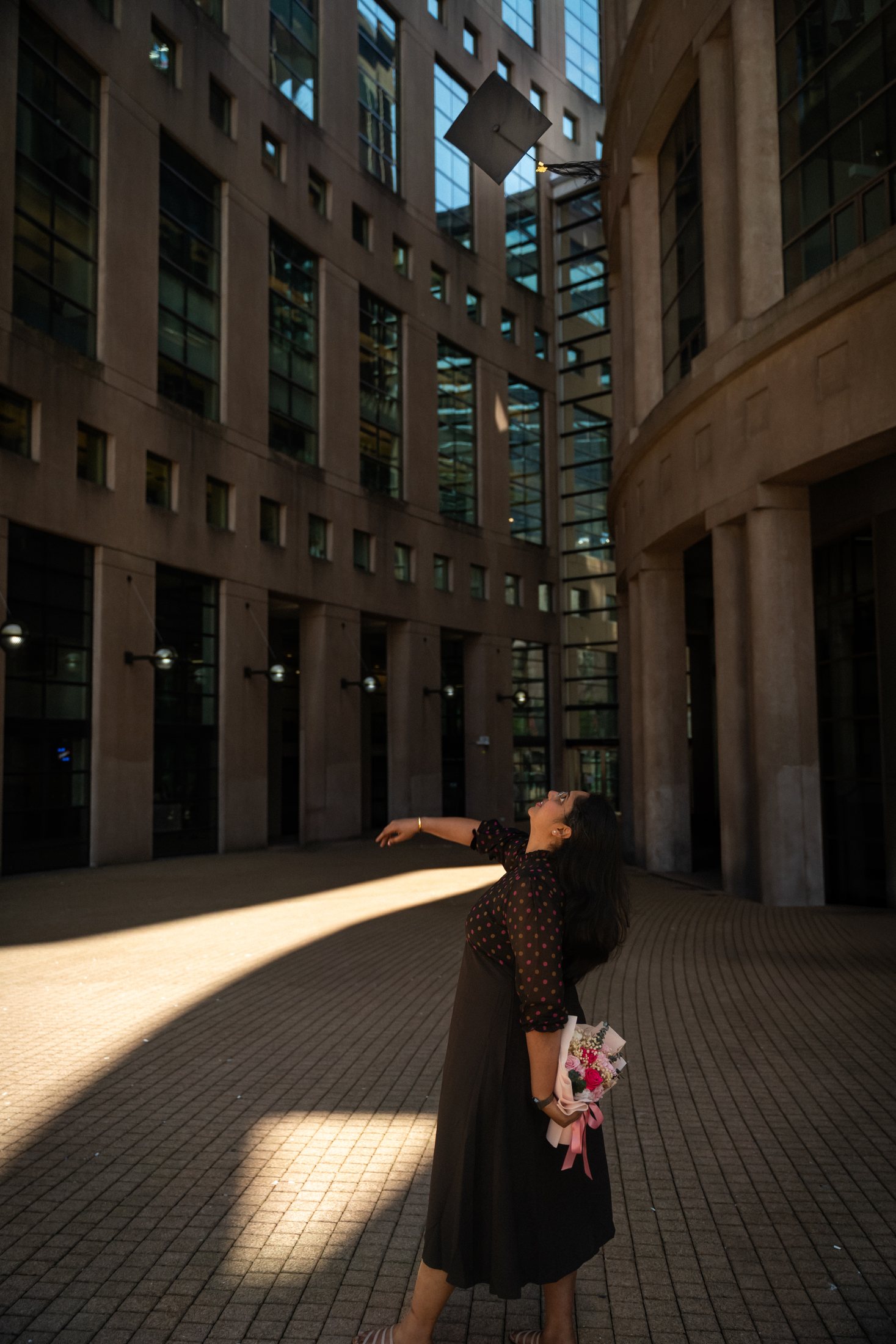 Graduate standing in a single shaft of afternoon light in the colonnade of Vancouver Public Library